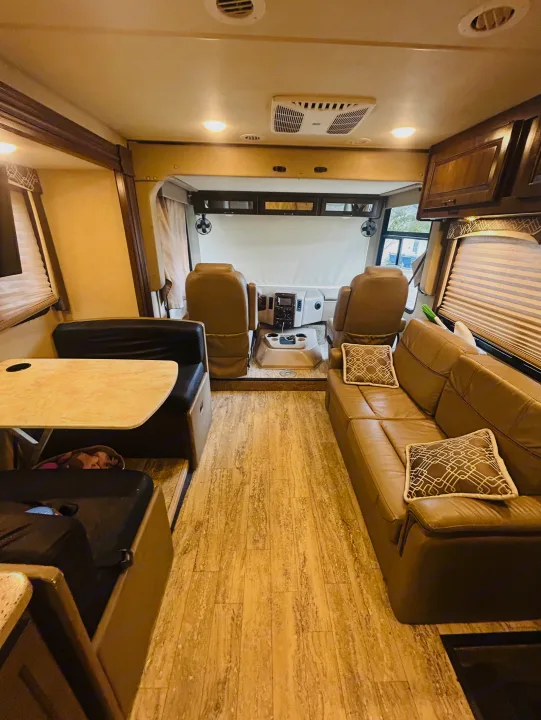 Interior view of an RV rental, showing the dinette, sofa, and front cockpit, featuring light wood-look flooring.. Thor Hurricane 2018