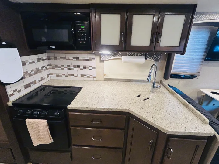 This modern and compact kitchen in an RV rental features a microwave, stove, sink, and ample countertop space.. Thor Hurricane 2018