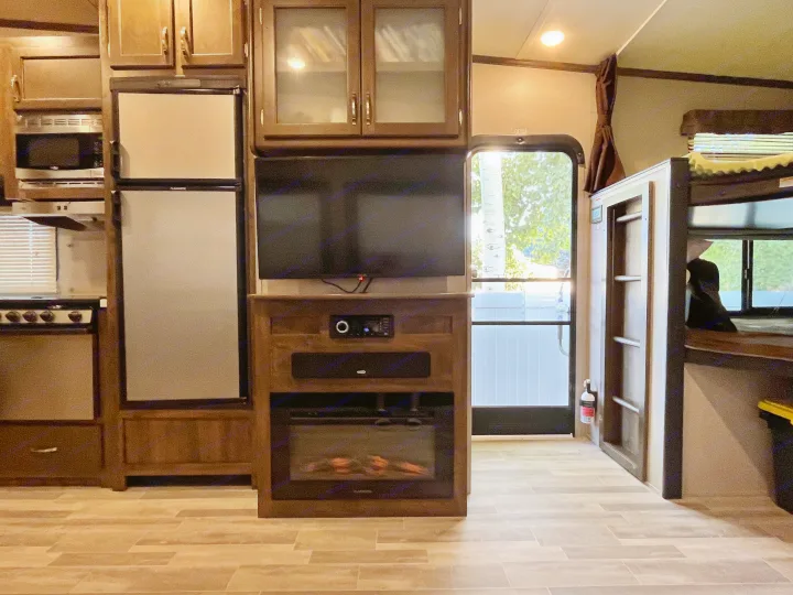 Explore this RV rental's cozy interior, featuring a full kitchen, entertainment center with fireplace, and spacious bunk beds for travel comfort.. Dutchmen Astoria 2018