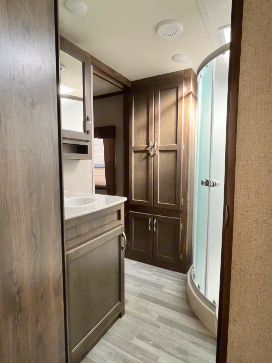 Clean RV rental bathroom featuring a wood vanity, sink, storage, and a modern curved shower.. Dutchmen Astoria 2018