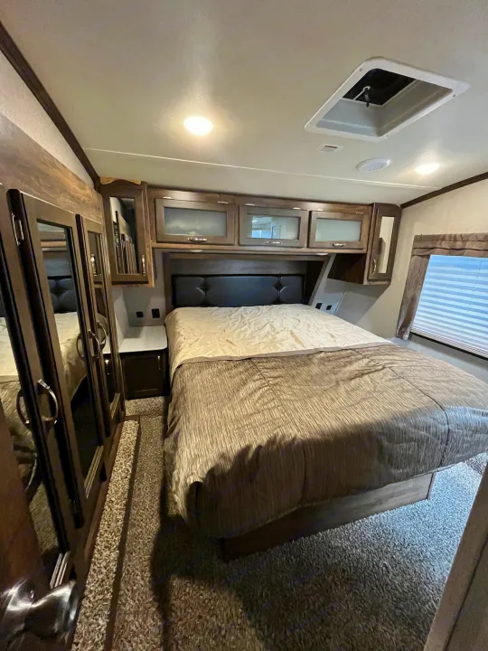 Explore this inviting RV rental bedroom featuring a queen bed, overhead cabinets, and mirrored wardrobes for a comfortable stay.. Dutchmen Astoria 2018