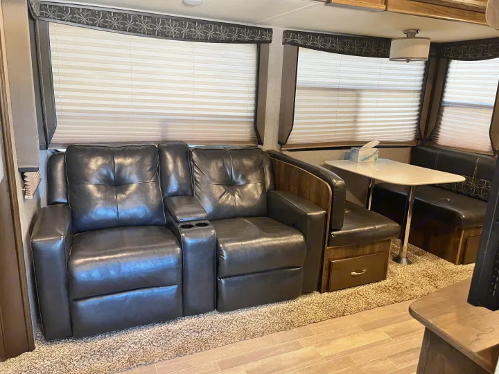 Inside an RV rental: dark leather recliners with cup holders, dinette with table, and light pleated blinds.. Dutchmen Astoria 2018