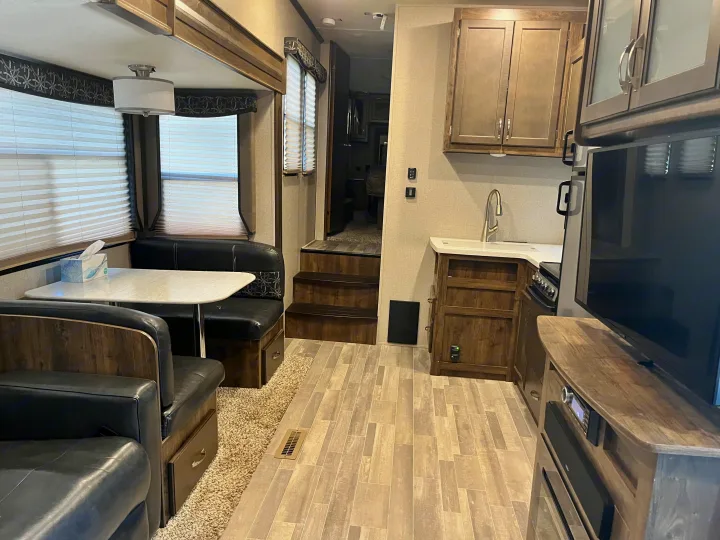 Modern RV rental interior showing a compact kitchen, dinette, and living area with wood-look flooring.. Dutchmen Astoria 2018