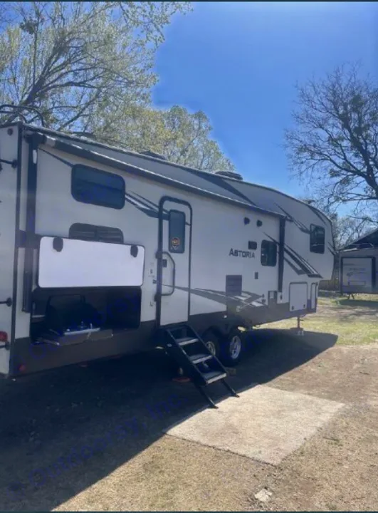 This Astoria fifth-wheel RV rental is parked at a campsite, featuring an outdoor grill and entry steps.. Dutchmen Astoria 2018