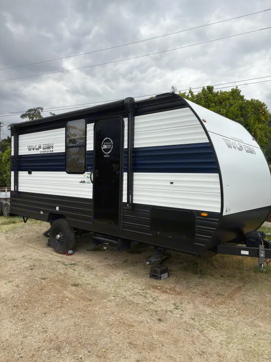 A black and white Wolf Den Cherokee travel trailer parked on a gravel lot under cloudy skies, perfect for an rv rental adventure.. Forest River Cherokee Wolf Den 16EV 2024
