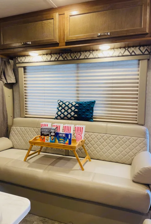 An RV rental interior featuring a cozy sofa with a bed tray holding popcorn and s'mores for a movie night.. Gulf Stream Conquest 2020