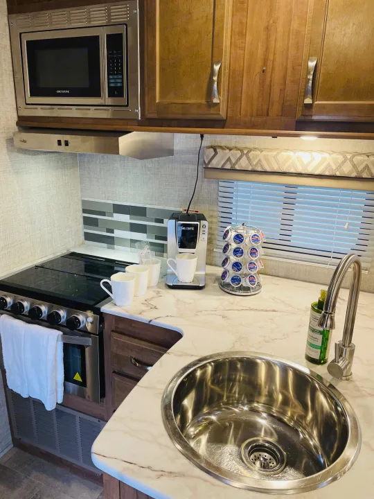 Modern RV rental kitchen with stainless steel appliances, sink, and coffee bar.. Gulf Stream Conquest 2020