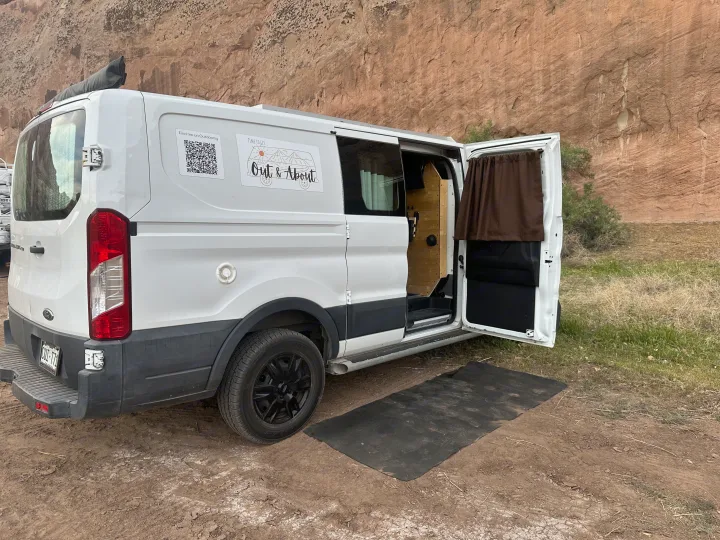 White custom RV rental camper van parked in nature with its side door open, inviting outdoor adventure.. FORD TRANSIT 250 2015