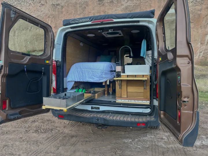 Custom RV rental camper van interior: cozy bed, pull-out kitchen with stove, and sink ready for adventures.. FORD TRANSIT 250 2015
