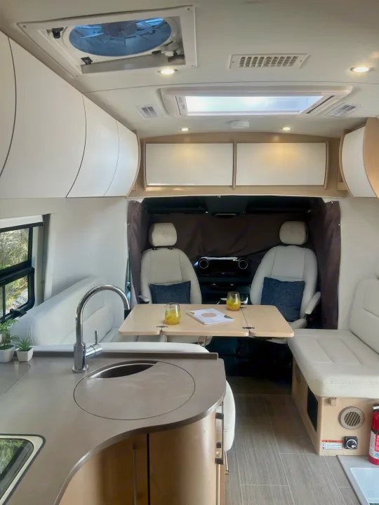 Spacious and modern RV rental interior featuring a kitchen, dining area, and comfortable seating. Perfect for road trips!. Leisure Travel Vans Serenity 2022
