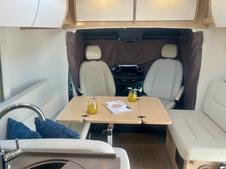 Spacious RV rental interior featuring a central dining table, comfortable lounge, and front cabin seats. Perfect for a relaxing trip.. Leisure Travel Vans Serenity 2022