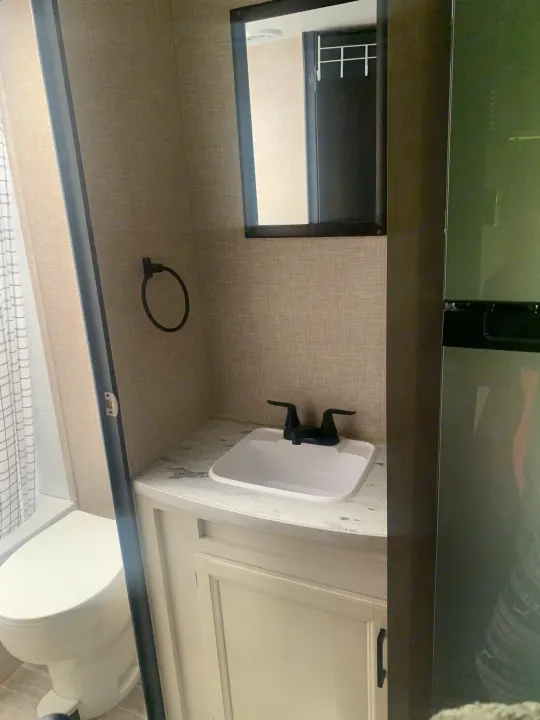 Inside a modern **RV rental**: a compact bathroom featuring a vanity with sink, mirror, and toilet, next to a shower area.. Jayco Jay Flight 2023