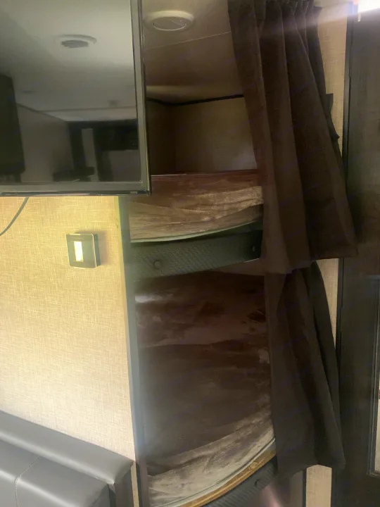 RV rental interior: stacked bunk beds with dark privacy curtains. A TV and thermostat are on the left.. Jayco Jay Flight 2023