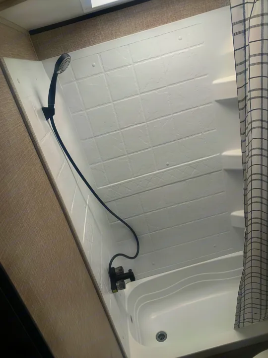 RV rental compact white shower with handheld showerhead, faucet, and a black & white plaid curtain.. Jayco Jay Flight 2023