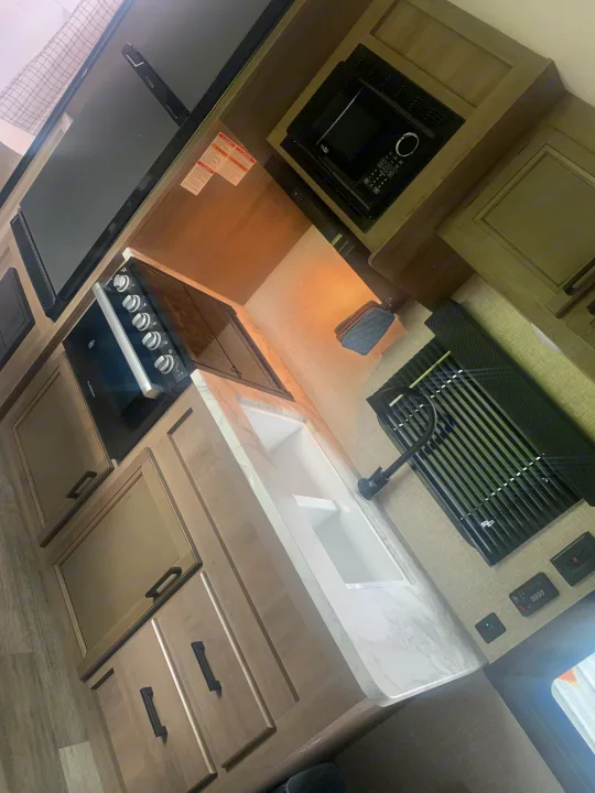 Clean RV rental kitchen: white marble-look counters, double sink, microwave, gas stove, light wood cabinets.. Jayco Jay Flight 2023