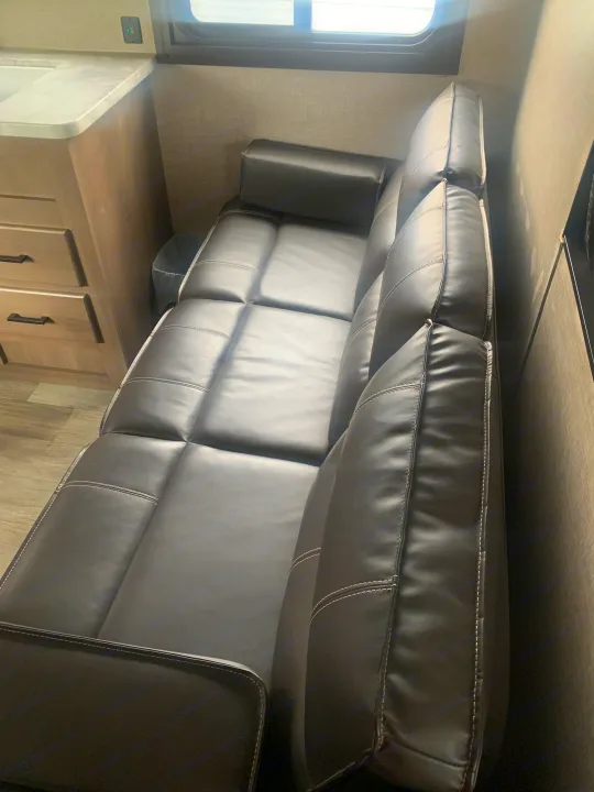 Experience comfort in this RV rental with a stylish black leatherette sofa, showing detailed stitching and nearby cabinetry.. Jayco Jay Flight 2023