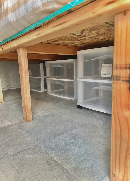 Under-bed storage in an RV rental: clear plastic drawers are neatly organized on a grey floor, seen from a low angle under wooden beams.. Coachmen 226 BH 2019