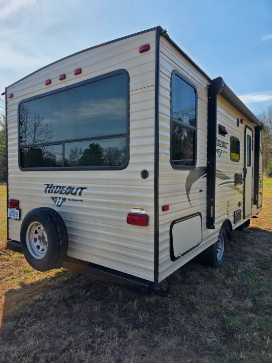 Rear view of a tan Hideout travel trailer RV with a spare tire, ready for an RV rental adventure in the outdoors.. Keystone RV Hideout LHS Mini 2017