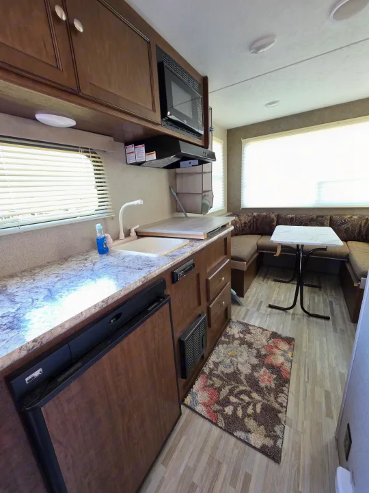 RV rental interior: Kitchenette with sink, microwave, refrigerator, and a dinette with table & bench seating.. Keystone RV Hideout LHS Mini 2017