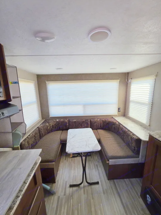 RV rental interior: A spacious U-shaped dinette area with patterned cushions, a white marble-look table, and large windows.. Keystone RV Hideout LHS Mini 2017
