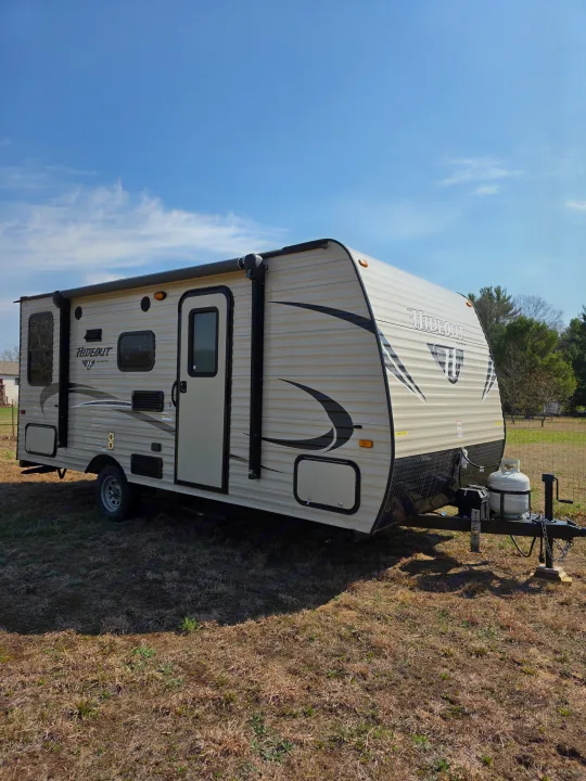 RV rental ready: A modern travel trailer with awning, parked in a sunny field, perfect for camping adventures.. Keystone RV Hideout LHS Mini 2017