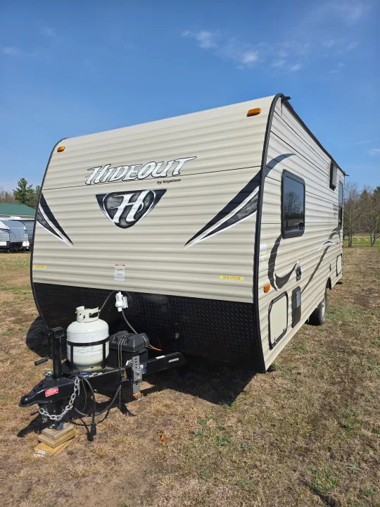 Beige Hideout by Keystone RV rental travel trailer with propane tank, parked in a sunny field.. Keystone RV Hideout LHS Mini 2017