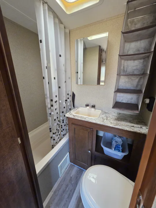 Inside an RV rental bathroom featuring a shower with curtain, toilet, vanity, and convenient hanging storage.. Keystone RV Hideout LHS Mini 2017