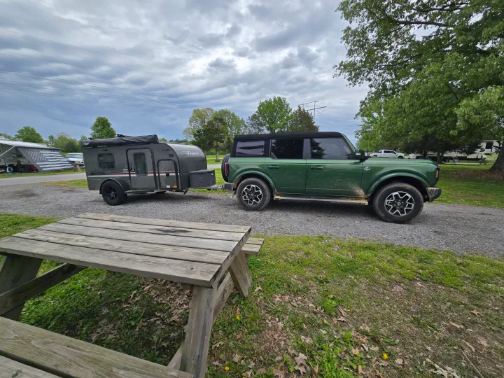 Green Bronco and a tear-drop RV rental trailer parked at a gravel campsite with a picnic table. Perfect for camping adventures.. InTech RV InTech RV Trailer 2021