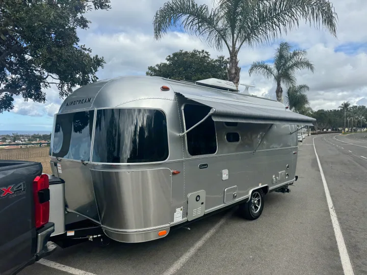 This silver Airstream travel trailer, an RV rental, is set up with awning extended, parked on a scenic coastal overlook.. Airstream 22' Airstream Caravel 2025