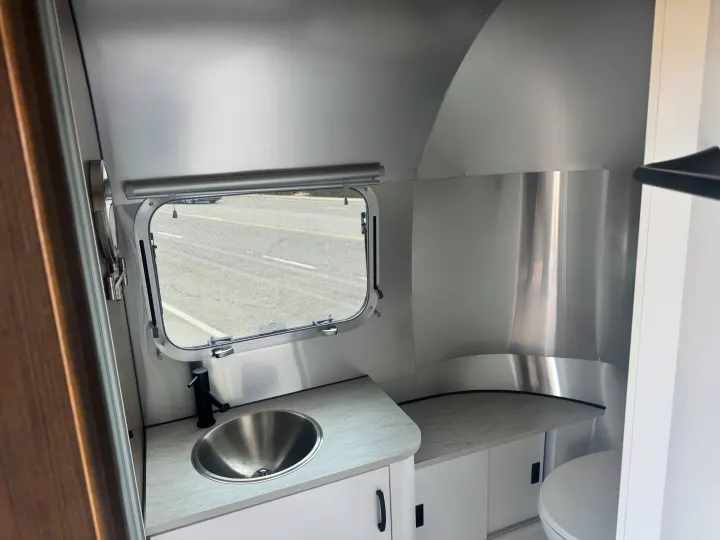 RV rental bathroom/kitchenette: a sleek silver sink, black faucet, light counters, and white cabinets in a compact, modern design.. Airstream 22' Airstream Caravel 2025