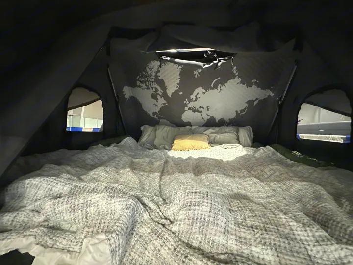 Cozy rv rental interior: a bed with a textured blanket and pillows, highlighted by a world map headboard. Ready for travelers.. Ford Ford F150 2024