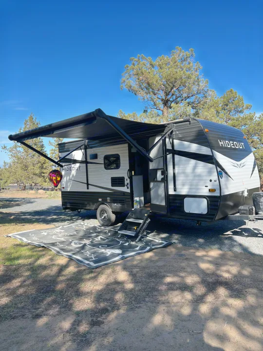 This Hideout travel trailer (RV rental) is set up for a relaxing day at the campsite, complete with an extended awning and outdoor mat.. Keystone RV Hideout 2021