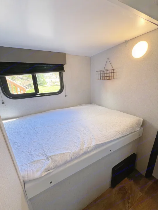 Cozy RV rental bedroom features a comfy bed, window view, textured walls, and wall basket.. Keystone RV Hideout 2021