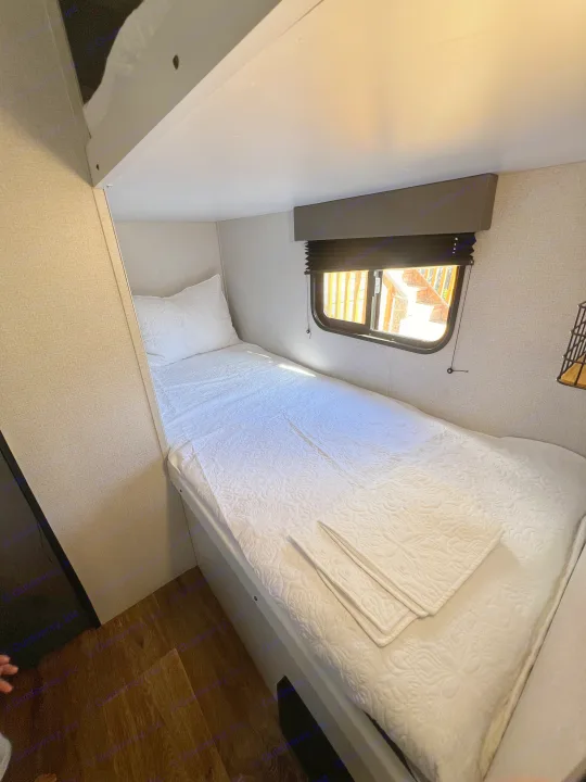 Cozy RV rental bunk bedroom with a single bed, white quilted bedding, and a window providing natural light.. Keystone RV Hideout 2021
