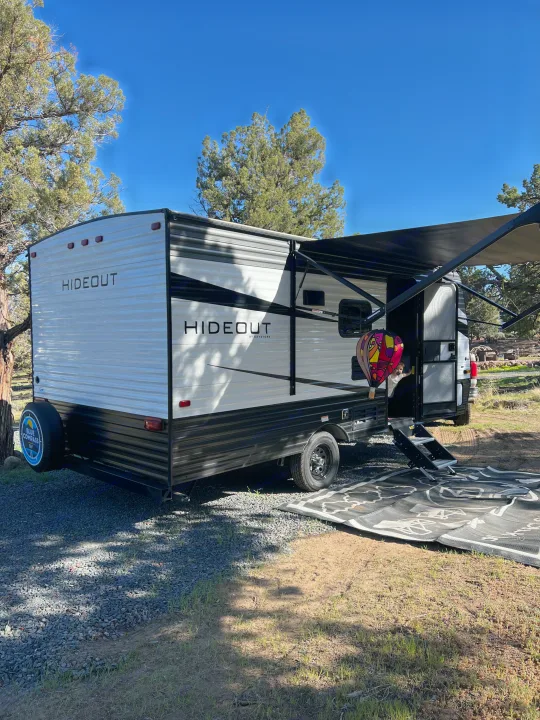 Bright day for an RV rental adventure! Our Hideout travel trailer, with awning & mat, and a child peeking out.. Keystone RV Hideout 2021