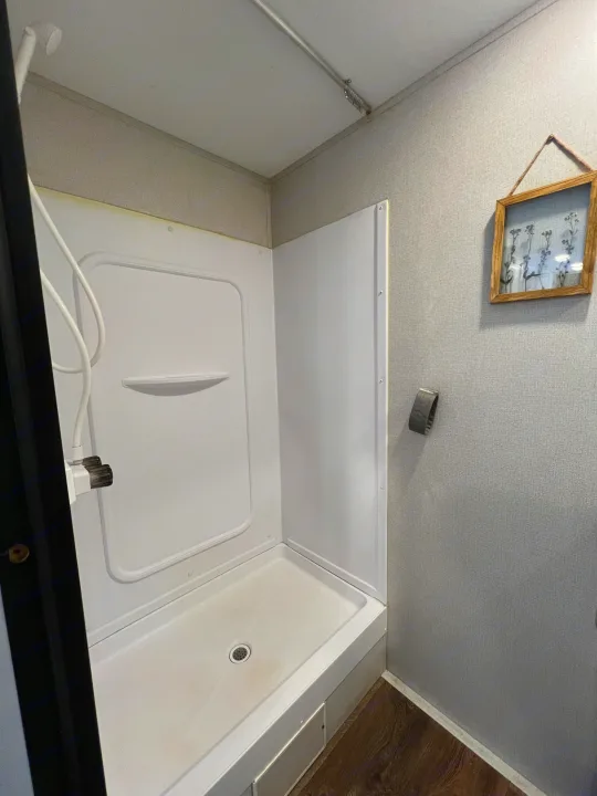 Inside an RV rental: a compact bathroom featuring a white shower stall, wood-look floor, and light grey textured walls.. Keystone RV Hideout 2021