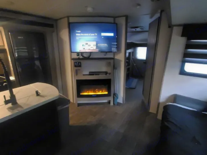 Modern RV rental interior: kitchen island, living space with fireplace, TV, and bunks visible down the hall.. Forest River Cherokee Alpha Wolf 2021