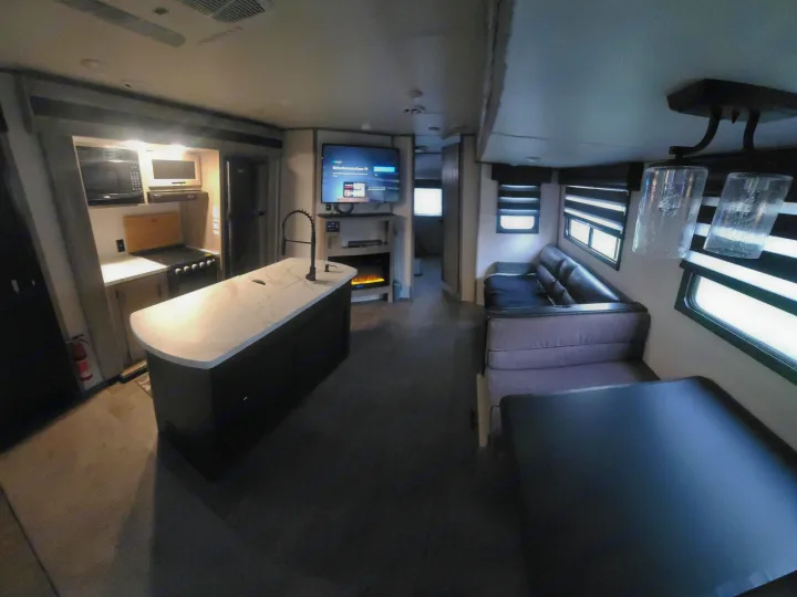 This RV rental interior features a modern kitchen island, cozy living area with TV/fireplace, and a comfortable dining space.. Forest River Cherokee Alpha Wolf 2021