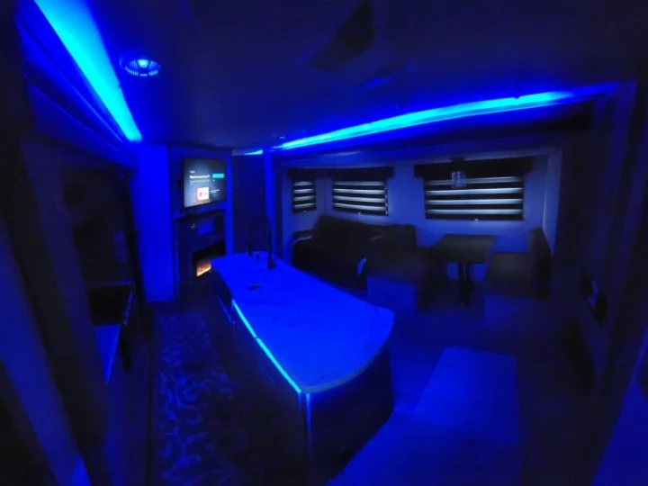 Experience this modern RV rental interior with vibrant blue LED lighting, a sleek kitchen island, and cozy living/dining areas.. Forest River Cherokee Alpha Wolf 2021