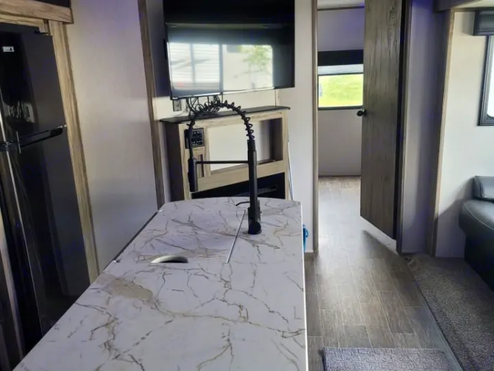 Modern RV rental interior showcasing a kitchen island with faucet, fridge, TV, and cozy living area.. Forest River Cherokee Alpha Wolf 2021