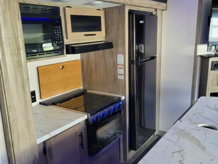 Modern RV rental kitchen with microwave, refrigerator, and stovetop for comfortable and convenient travel cooking.. Forest River Cherokee Alpha Wolf 2021