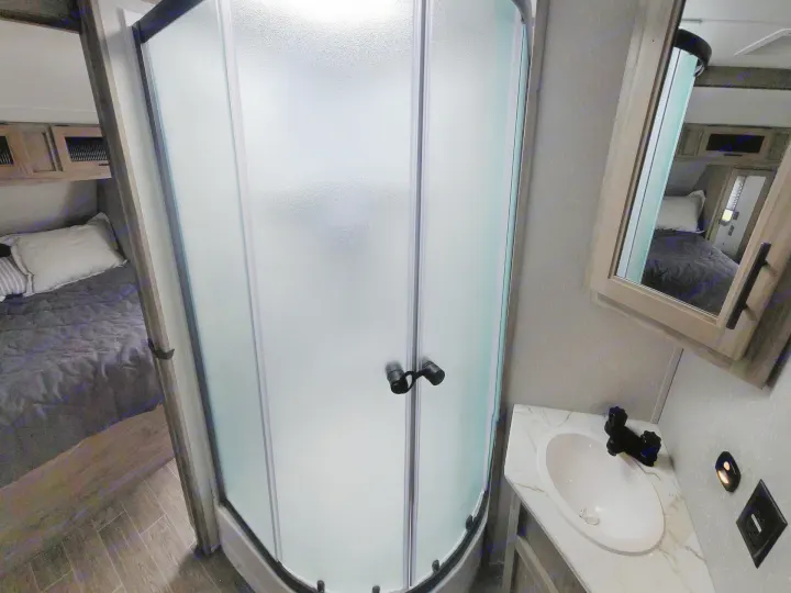 Inside an RV rental: a compact bathroom with a frosted glass shower, vanity sink, and the bedroom visible in the background.. Forest River Cherokee Alpha Wolf 2021