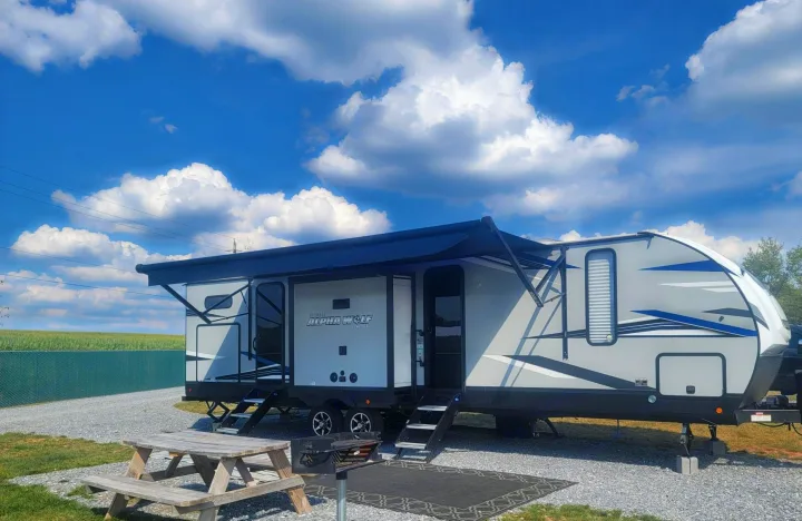 Cherokee Alpha Wolf travel trailer RV rental with awning extended, parked at a sunny gravel campsite.. Forest River Cherokee Alpha Wolf 2021