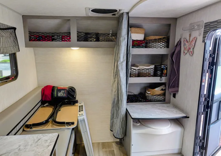 This RV rental interior features a bunk bed, organized storage shelves, and a convenient portable toilet for a compact camper setup.. Coachmen Viking 1200ROK 2025