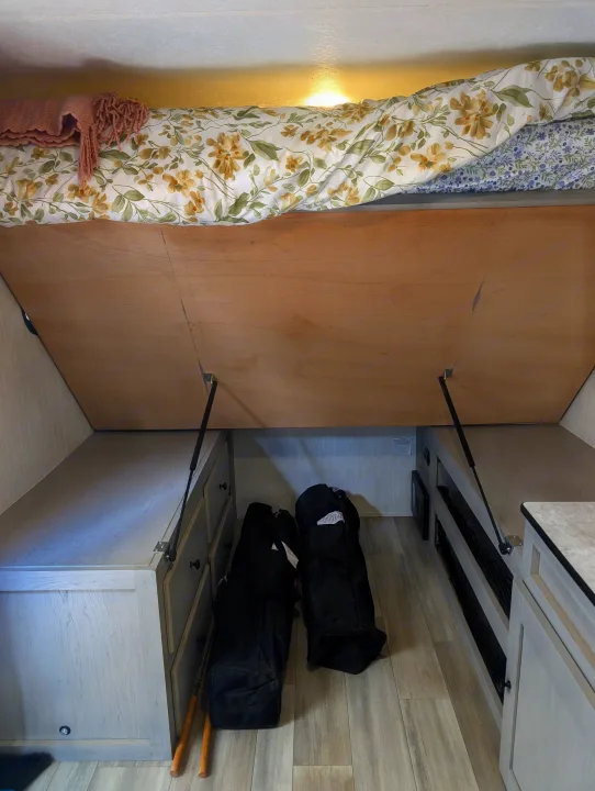 RV rental interior: Lift-up bed reveals ample under-bed storage with built-in cabinets, perfect for compact living.. Coachmen Viking 1200ROK 2025