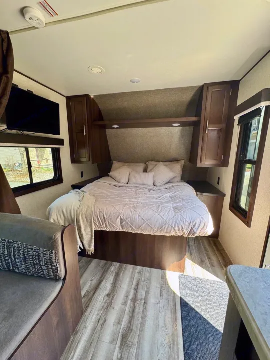 Cozy RV rental bedroom featuring a comfortable bed, overhead storage, TV, and light wood-look flooring.. Jayco Jay Flight SLX 2019