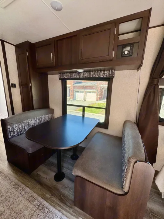 Inside an RV rental, a cozy dinette features dark wood cabinets, a table, and upholstered benches by a window.. Jayco Jay Flight SLX 2019