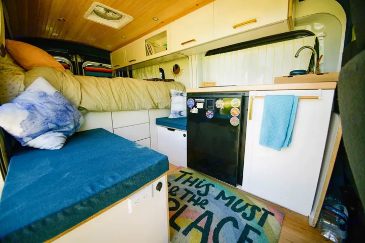 Cozy camper van interior. Perfect for an RV rental adventure, featuring a bed, kitchen, and seating area.. Ford Transit 2019