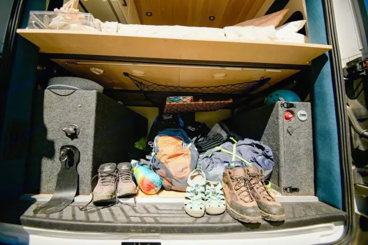 RV rental storage: Organized camper van trunk showing bed, outdoor gear, hiking boots, and power station for adventures.. Ford Transit 2019