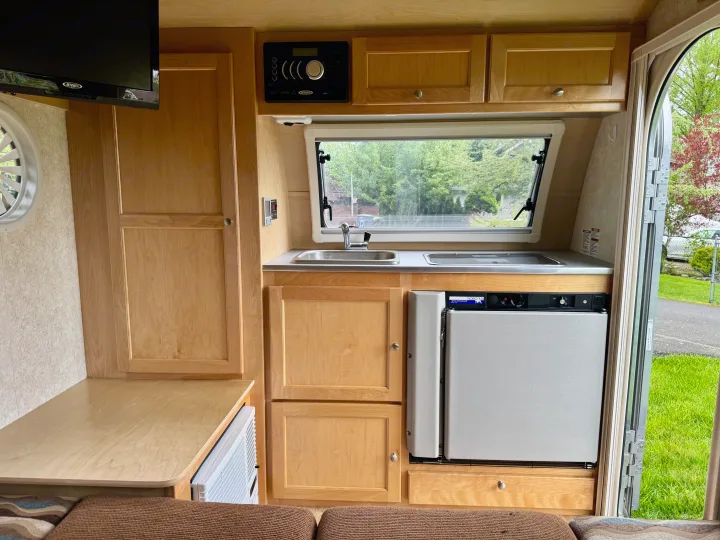 Compact rv rental interior with light wood cabinetry, a kitchenette (sink, cooktop), Norcold fridge, Jensen TV/stereo, and comfy seating.. Pleasant Valley/NuCamp T@B 2016